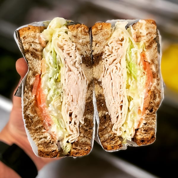 A Delite Cafe and Deli Taylor turkey sandwich, cut in half, revealing layers of meat, lettuce, and tomato.