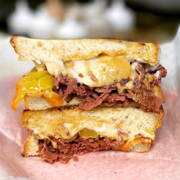 Close-up of a Delite Cafe and Deli Taylor sandwich with meat, melted cheese, and peppers.