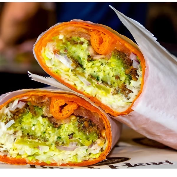 Two halves of a Delite Cafe and Deli Taylor sandwich wrap with green filling and orange tortilla.