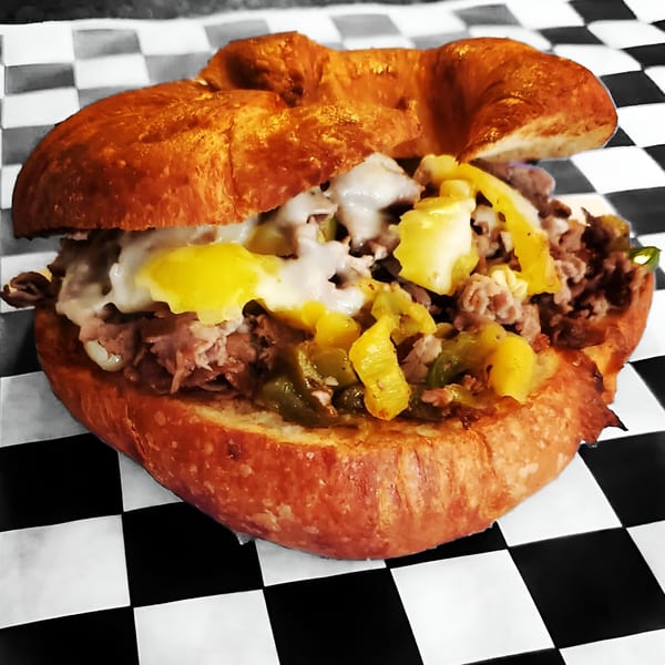 A Delite Cafe and Deli Taylor sandwich with meat, melted cheese, and peppers on a croissant.