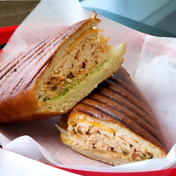 A grilled panini sandwich from Delite Cafe and Deli Taylor, cut in half, revealing chicken, cheese, and lettuce.