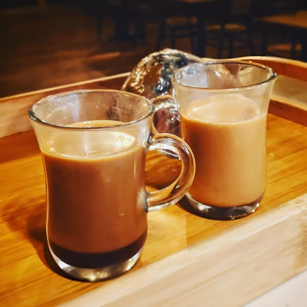 Two glasses of chai tea, one dark and one light, on a wooden tray at Delite Cafe and Deli.